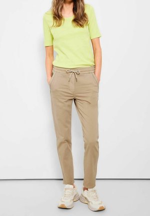 Lichtgroene top met korte mouwen gecombineerd met beige joggers met koord in de taille en crèmekleurige sneakers. Casual, losse pasvorm.