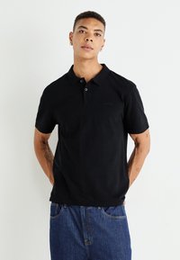 Crna majica polo kratkih rukava od pamuka s ovratnikom, sa suptilnim Levi's logotipom na prsima, uparen sa plavim trapericama.