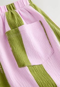 Multicolor stof med grønne og pink striber. Har en tekstureret overflade og en lappetaske med synlige syninger.