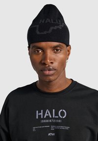 Zwarte gebreide muts met een klep en een grijs "HALO" logo ontwerp. Draagt een zwart shirt met grijze tekst en grafische details.