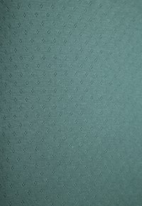 Teal stof met een fijne geribde textuur en kleine, herhalende ruitpatronen. Zachte en gladde oppervlakte.