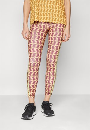 Leggings med et lilla og gult mønster av sammenkoblede former, supplert med grønne sidelister. Laget av elastisk, glatt stoff.
