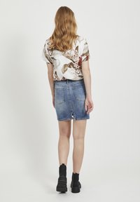 Jupe en denim mini avec un ourlet brut et une fente à l'arrière, assortie à un haut à manches courtes à motifs floraux dans des couleurs claires. Bottines noires.