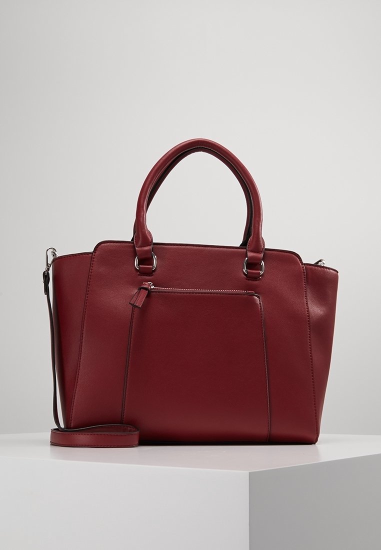 Czerwona skórzana torebka z dwoma uchwytami, odpinanym paskiem na ramię, przednią kieszenią na suwak oraz wyraźnie zarysowanym, prostokątnym kształtem. Gładka faktura i minimalna liczba szwów.