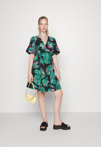 Vestido com estampa floral apresentando folhas verdes e flores cor-de-rosa sobre um fundo preto, com mangas bufantes e uma saia em camadas. Acompanhado de uma bolsa amarela.
