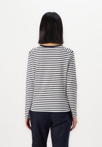 Langarm gestreept shirt met marineblauwe en crèmekleurige horizontale strepen, ronde halslijn en zachte, gestructureerde stof. Draagt in combinatie met donkere broek.