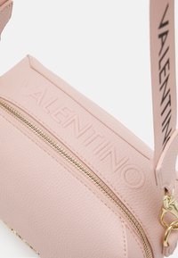 Rožinė oda kuprinė su tekstūruota paviršiumi, iškilmingas logotipas priekyje, auksinė užtrauktuko uždarymo sistema ir nuimamas diržas su prekės pavadinimu.