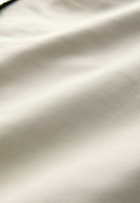 Cremefarvet stof med en glat tekstur og subtil glans. Vevet er tæt, hvilket viser et ensartet mønster gennem hele stoffet.