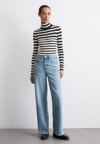 Zwart-witte gestreepte coltrui gecombineerd met lichtblauwe wijde jeans. Het model draagt zwarte plateau schoenen. Eenvoudig ontwerp, casual stijl.