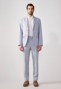 Lys grå rutete dress med to knapper, notche lapels og sidelommer, paret med en hvit skjorte og brune loafers.