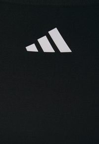 Črne športne legice z rebrasto teksturo in belim Adidasovim logotipom, ki prikazuje tri diagonalne črte v zgornjem levem kotu.
