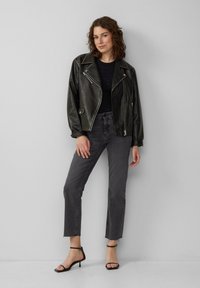 Veste de moto en cuir noir, haut noir ajusté avec des détails subtils, jean cropped gris, et sandales noires à lanières. Design simple et contemporain.