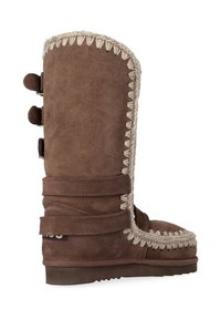 Stivale in suede marrone con rifinitura intrecciata. Presenta tre bottoni decorativi sul lato, una punta arrotondata e una suola piatta in gomma.