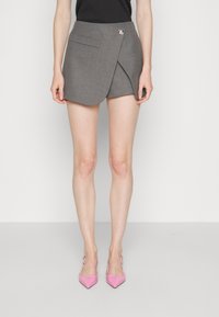 Jupe portefeuille grise avec une poche unique et une fermeture par bouton. Élégamment associée à des escarpins roses à bouts pointus, sur un fond neutre.