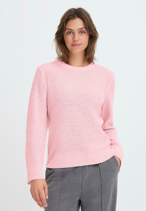 Maglione lavorato a maglia rosa chiaro con un motivo testurizzato, scollo rotondo e polsini a coste. Abbinato a pantaloni grigi, l'aspetto complessivo è informale.