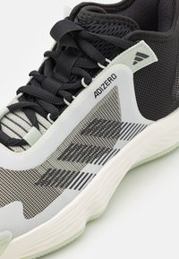 Närbild av en svart och grå Adidas Adizero löparsko med överdel i mesh, svarta snören och vit dämpad sula.