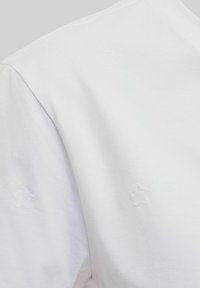 Vit bomullströja med präglade stjärnmönster. Mjuk textur med en enkel rundhalsdesign, minimalistisch och ren estetik.