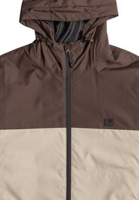 Brown and beige waterproof jacket with a hood, featuring toggles, a full front zipper, and a logo patch on the chest. Smooth texture.