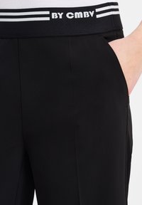Zwarte sportbroek met een brede zwarte tailleband met witte strepen en tekst, een gladde textuur en zijzakken.