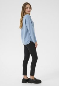 Maglione oversized blu chiaro con dettagli a coste, abbinato a jeans skinny neri e mocassini neri. Il maglione ha un orlo arrotondato e una vestibilità rilassata.