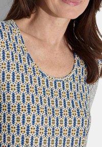 Korte mouw top met een ronde halslijn, witte basis met blauwe en gele bloemen- en geometrische patronen, en een zachte stoftextuur.