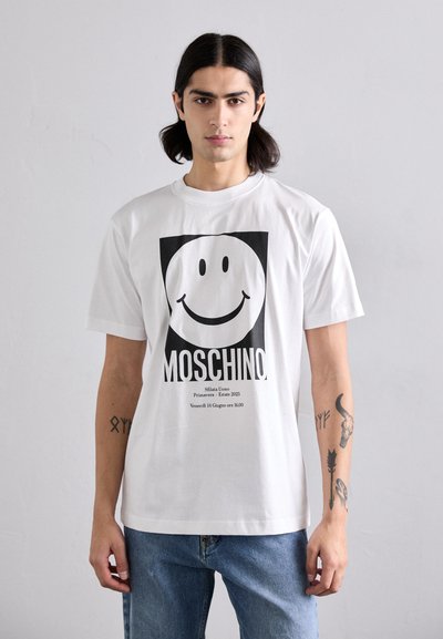 Witte t-shirt met korte mouwen met een grote zwarte glimlachende gezicht en de tekst "MOSCHINO". Gemaakt van katoen, met een relaxte pasvorm en een ronde hals.