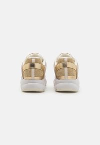Joggesko med et metallisk gull- og beige design, mesh-overdel, myke hvite såler og kontrasterende teksturerte detaljer på hælen.