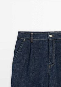 Dunkelblaue Jeans mit einem Knopfverschluss, Gürtelschlaufen und sichtbaren Seitentaschen-Nähten auf weißem Hintergrund.