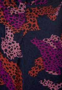 Tissu foncé avec un motif abstrait d'imprimé léopard en tons de violet, rose et orange rouille avec des taches noires.