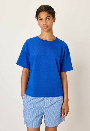 T-shirt in cotone blu con una vestibilità ampia, maniche corte e colletto a girocollo. Abbinata a pantaloni corti a strisce blu chiaro, con chiusura a bottoni.