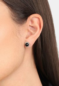 Pendientes de studs negros con un acabado brillante, rodeados por un círculo metálico plateado; forma redonda, tamaño pequeño, textura suave.