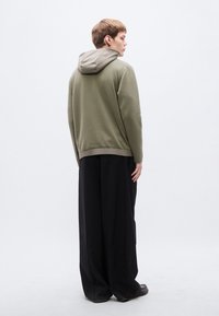 Χακί φούτερ με αντίθετη ανοιχτό γκρι κουκούλα, σε συνδυασμό με φαρδιά μαύρα παντελόνια. Ομαλή υφή, μινιμαλιστικός σχεδιασμός, χωρίς ορατά σχέδια.