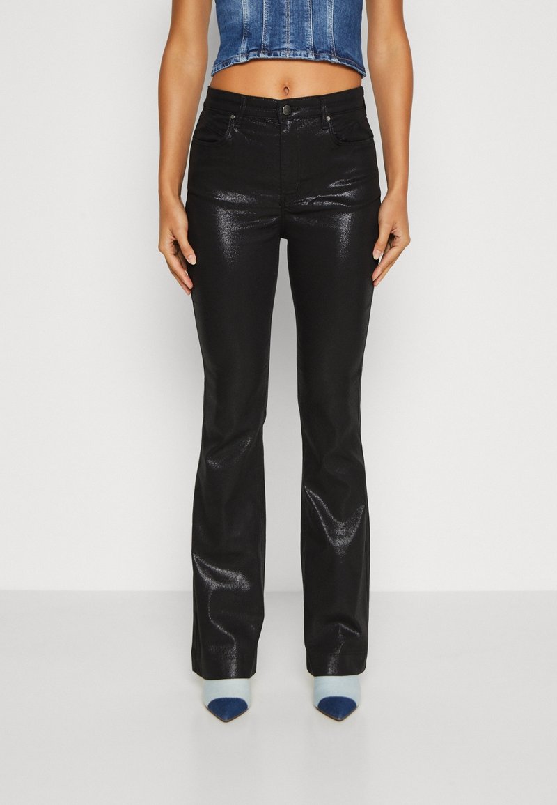 Femme portant un pantalon flare noir brillant à taille haute, un top court en denim bleu et des bottes à bout pointu avec un motif bleu et blanc.