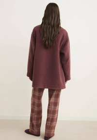 Chaqueta de forro polar color burdeos con corte relajado, combinada con pantalones de cuadros en tonos marrones y burdeos, con una textura suave.
