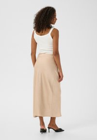 Jupe midi beige taille haute en tissu lisse et fluide, associée à un débardeur blanc et des mules noires à talons. Design simple, sans motifs.