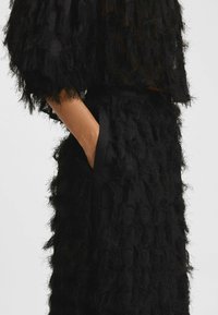 Outfit nero testurizzato composto da un top trasparente con fibre sfilacciate e una gonna coordinata, entrambi caratterizzati da una costruzione a strati e tasche.