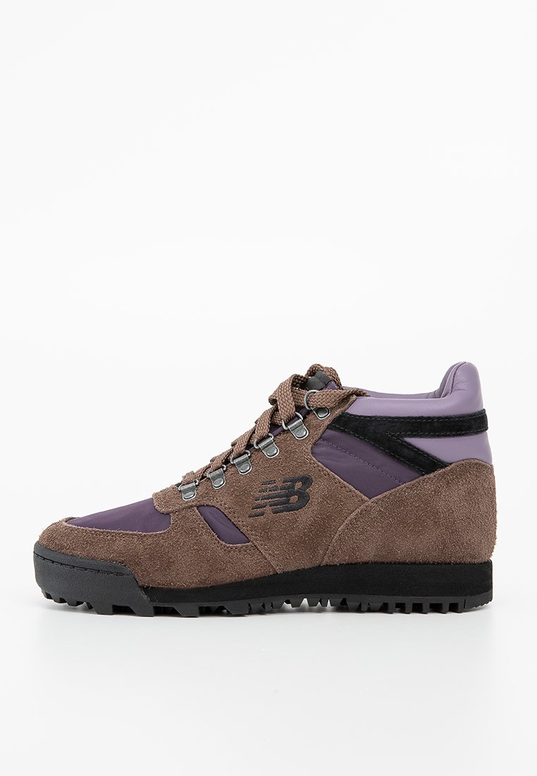Bruine en paarse wandelschoen van suède en synthetische materialen. Voorzien van metalen veterogen, een robuuste zwarte zool en het New Balance-logo op de zijkant.
