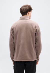 Καφέ φλις μπουφάν με ψηλό γιακά και ελαστικές μανσέτες, με απαλό υφή και άνετη γραμμή, σε προβολή από πίσω.