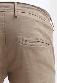 Beigefärgade bomullsbyxor med en bakficka med horisontell öppning och subtila sömnadsdetaljer. Slät textur med en skräddarsydd passform.