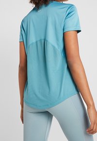 Ljusblå atletisk t-shirt med ett andningsbart meshnätpanel på baksidan, korta ärmar och rundad nederkant. Har en diskret Nike-logotyp vid halsringningen.