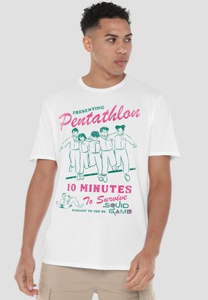 Weißes T-Shirt mit kurzen Ärmeln, das grafischen Text in Grün und Pink zeigt und Charaktere sowie verspielten Text in Bezug auf "Squid Game" darstellt.