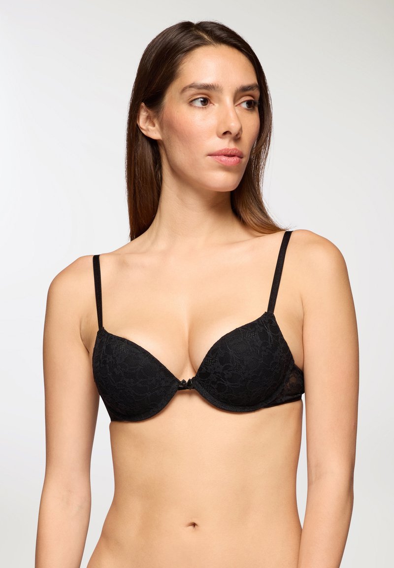 Bralette in pizzo nero con coppe imbottite a scollo profondo e spalline sottili regolabili. Presenta un piccolo dettaglio a fiocco centrale sulla parte anteriore.