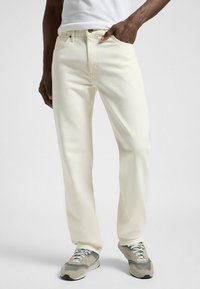 Jeans en coton blancs avec une coupe droite, dotés d'une poche avant, de coutures discrètes et d'une fermeture à boutons classique. Associés à des baskets grises.