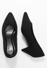 Escarpins compensés en daim noir à bout pointu avec une texture lisse, dotés d'un talon compensé bas et sans accessoires ou accents visibles.