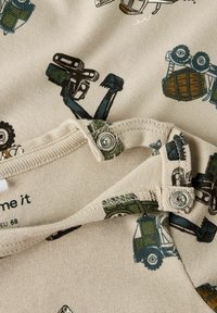 Baumwoll-Overall mit beigefarbenem Hintergrund und bedruckten Illustrationen von Baustellenfahrzeugen in Dunkelgrün und Blau. Druckknopfverschluss am Ausschnitt.