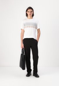 Weißes T-Shirt mit horizontalen grauen und pinken Streifen auf der Brust, kombiniert mit schwarzen Hosen und einer schwarzen Ledertasche. Glatte Textur.