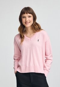 Roze V-hals trui gemaakt van zachte stof met lange mouwen, met een klein zwart geborduurd figuurtje op de borst. Casual pasvorm.