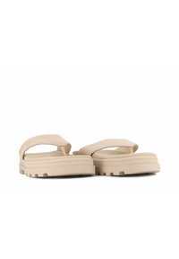 Beige flip-flops dengan loop jari yang lembut dan sol yang empuk. Sol tebal dengan pegangan tekstur dan desain yang bersih serta minimalis.