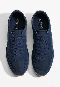 Sötétkék sportcipők szövet felsőrésszel, texturált fűzőkkel és barna gumi talppal. Jellemzője a logóval ellátott talpbetét és a megerősített orr.