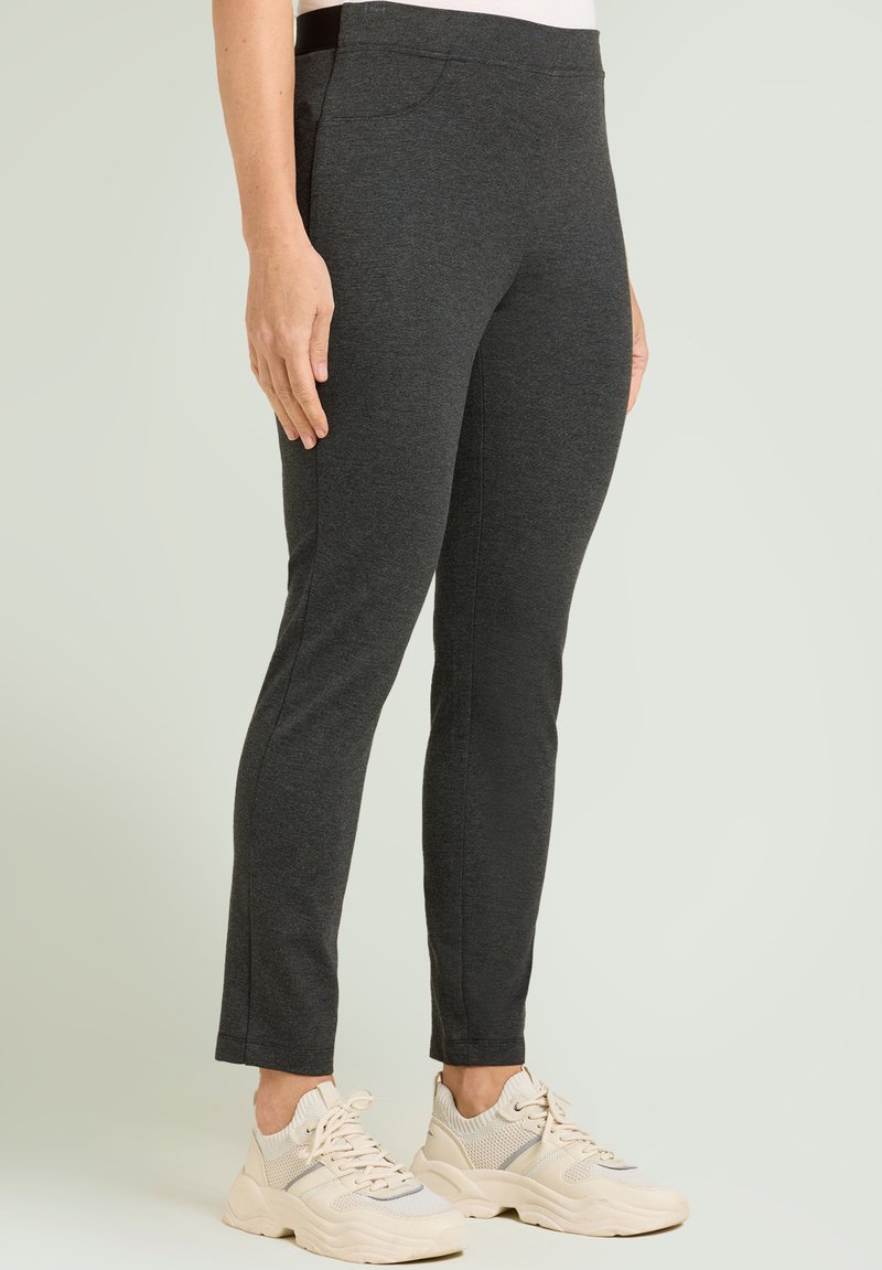 Leggings gris oscuro hechos de material elástico, con una textura suave, ajuste ceñido y bolsillos en los costados. Combinados con zapatillas de color claro.